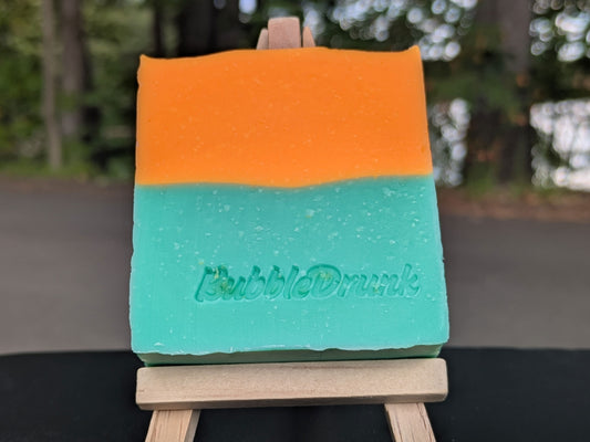 A handmade bar of soap that is orange and green, and scented with Fresh Squeezed Orange Juice, Juniper, and Gin fragrances. Juice & Gin was made from 100% organic oils.
