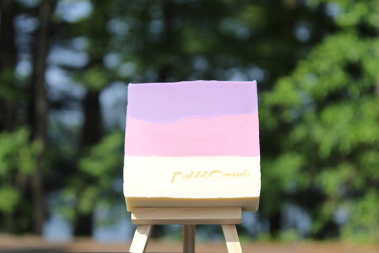 A handmade bar of soap that is purple, pink, and white, and scented with Black Raspberry, Vanilla, and Champagne fragrances. Mother In Law's Favorite was made from 100% organic oils.