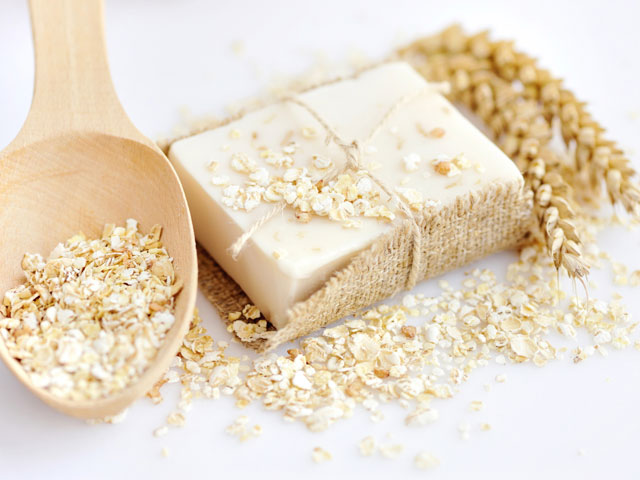 A bar of Oatmeal Soap next to a wooden spoon full of oats
