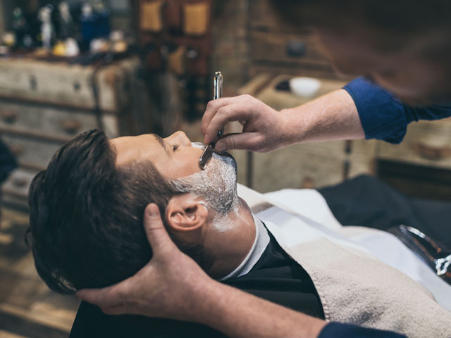 A barber shaving a man's shaving soap lathered beard with a flat razor