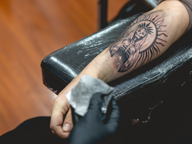A tattoo artist patting an arm tattoo with a clean paper towel